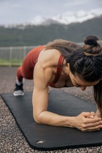 Vrouw houdt een plank aan op een yogamat buiten, met bergen op de achtergrond