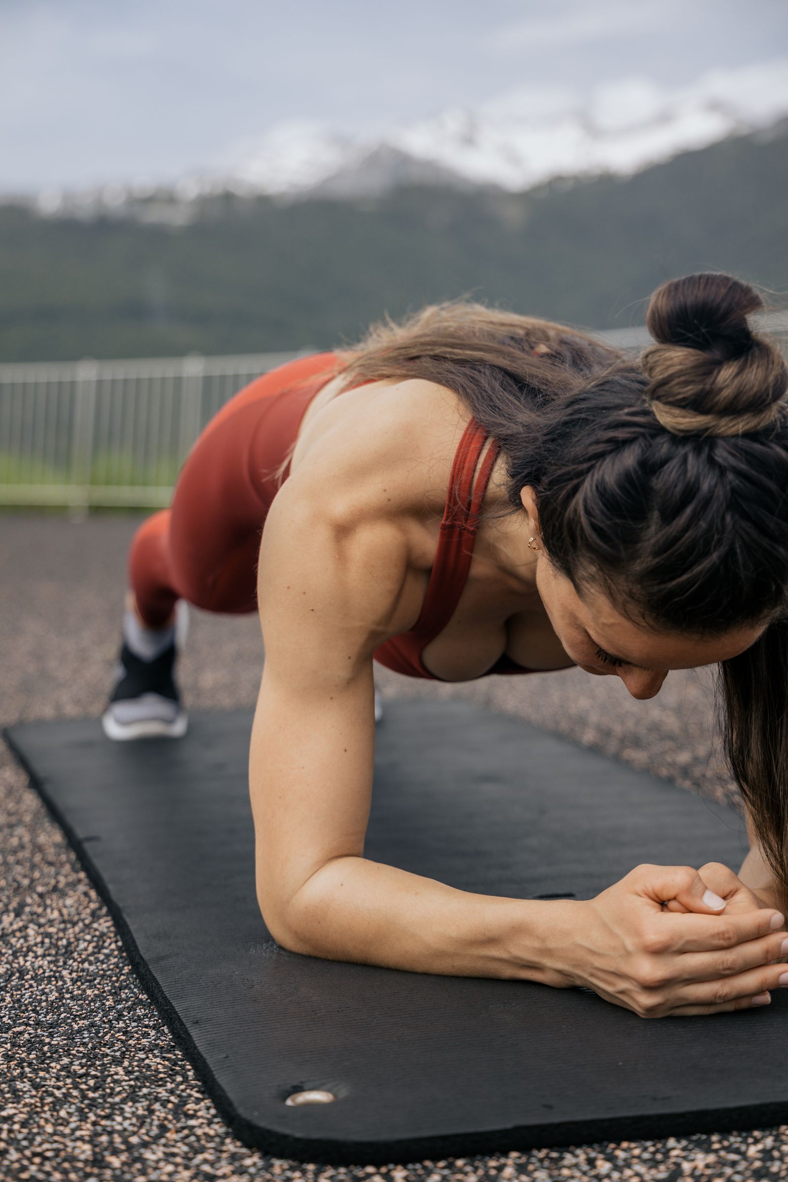 Vrouw houdt een plank aan op een yogamat buiten, met bergen op de achtergrond