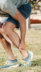 Hardloper in sportschoenen pakt zijn onderbeen vast en twijfelt of het spierpijn is of een blessure