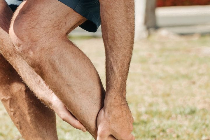 Hardloper in sportschoenen pakt zijn onderbeen vast en twijfelt of het spierpijn is of een blessure
