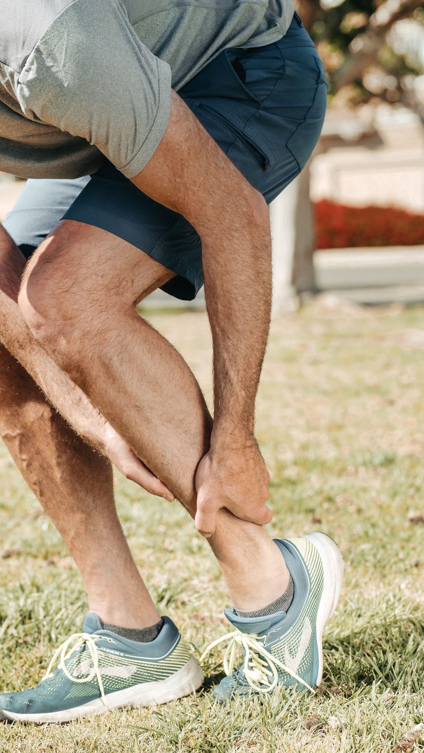 Hardloper in sportschoenen pakt zijn onderbeen vast en twijfelt of het spierpijn is of een blessure